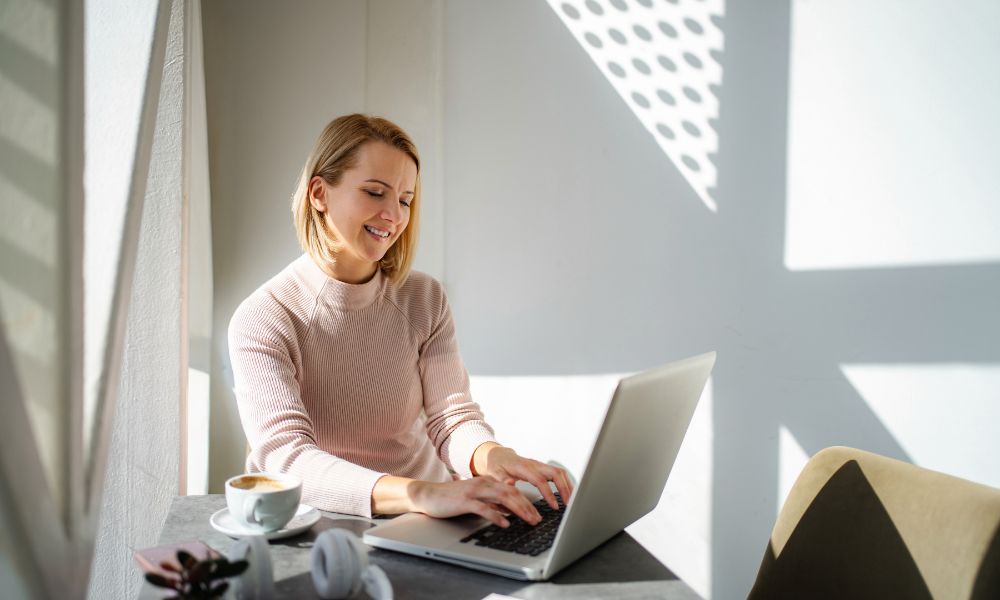 Teacher at laptop smiling — warm, modern classroom setting. Shows productivity and positivity.